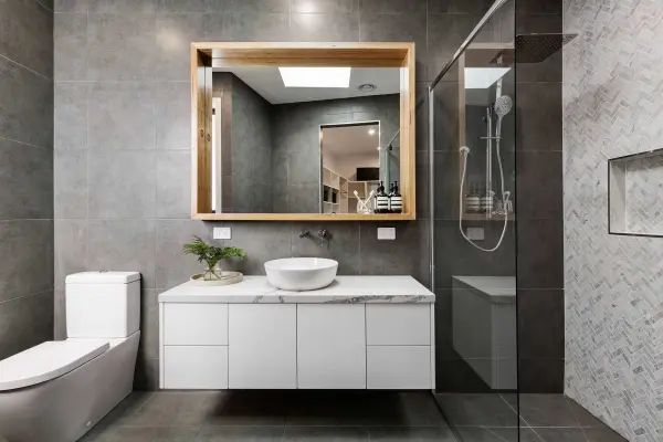 Phòng tắm hiện đại với bồn cầu, lavabo trên tủ, gương lớn và vòi sen trong suốt.